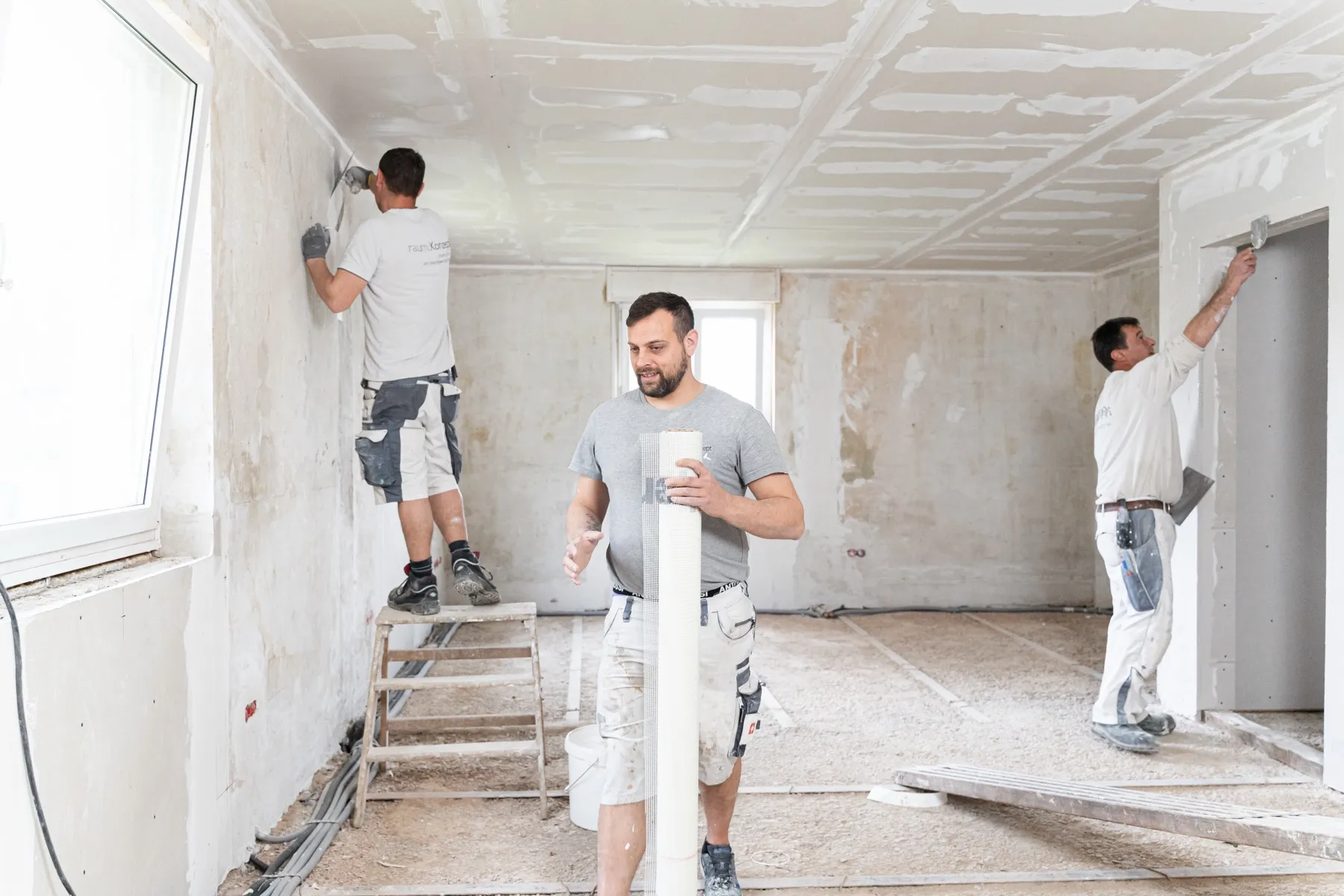 Drei Maler von raum.Konzept verputzen und spachteln einen Altbau-Raum